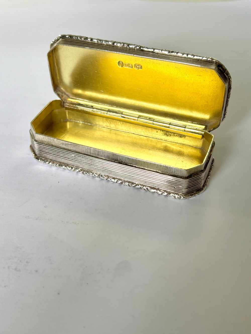 An open rectangular William IV silver gilt snuff box featuring reeded side panels, chased borders, and clear silver hallmarks inside the gilded lid.