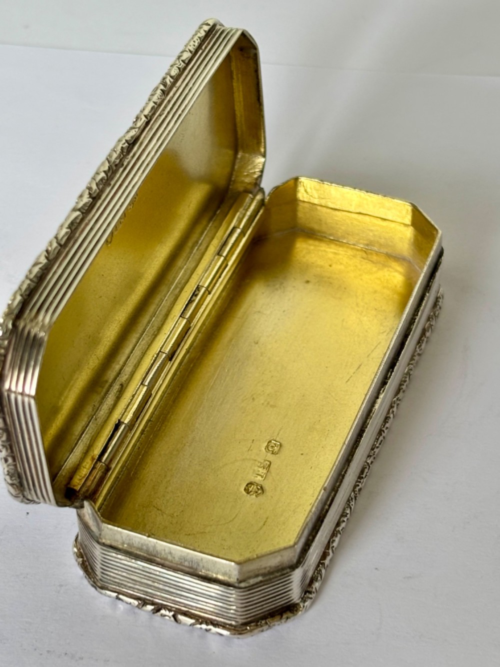 An open rectangular William IV silver gilt snuff box featuring reeded side panels, chased borders, and clear silver hallmarks inside the gilded lid. View VI