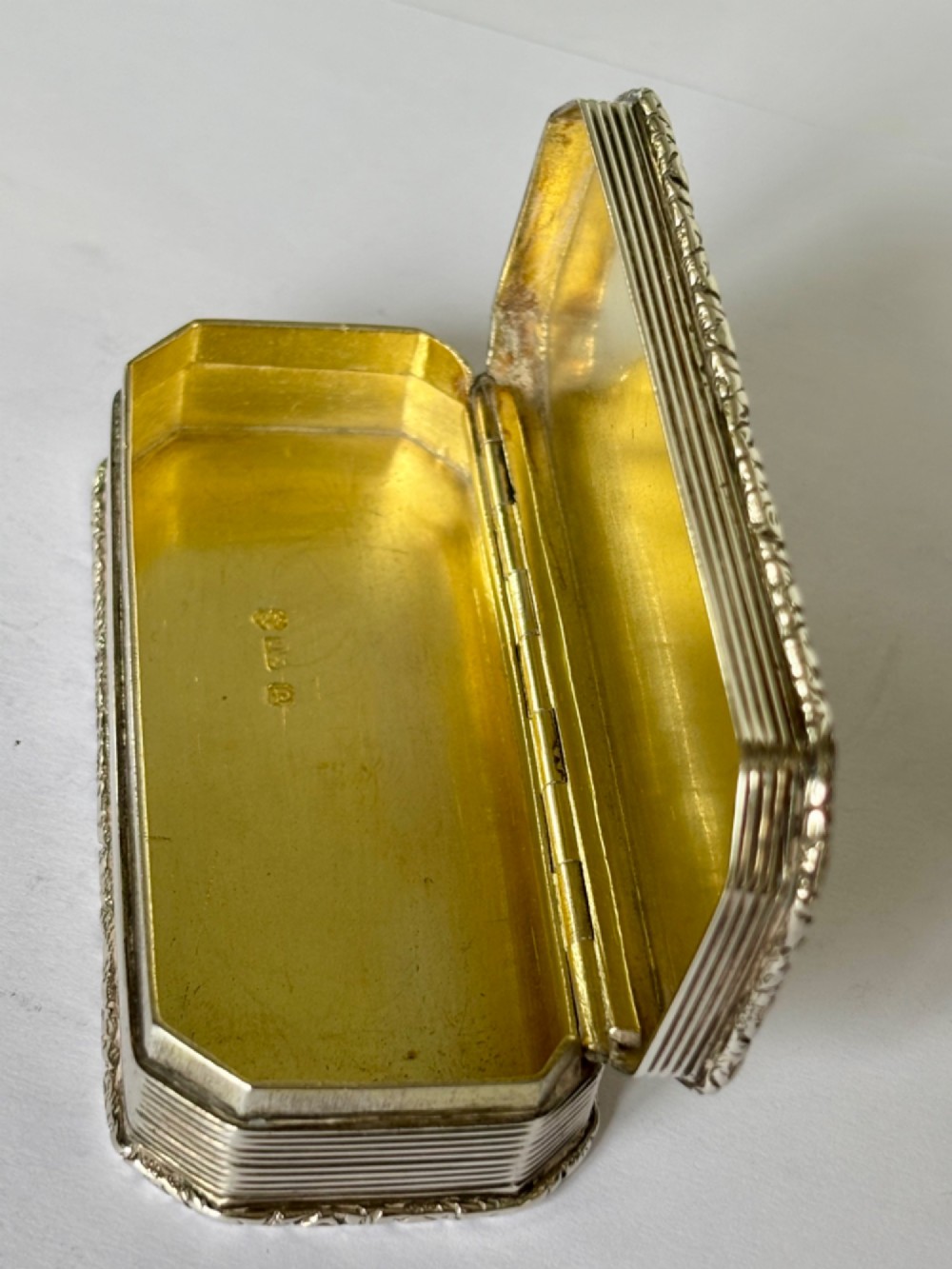 An open rectangular William IV silver gilt snuff box featuring reeded side panels, chased borders, and clear silver hallmarks inside the gilded lid. View VII