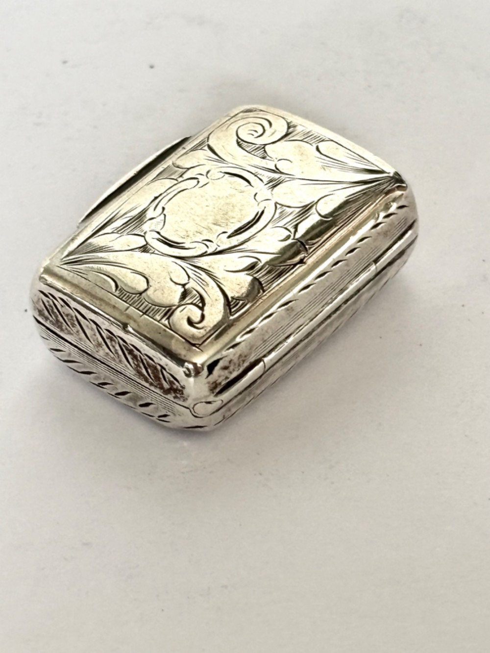 An early Victorian rectangular sterling silver vinaigrette featuring intricate foliate scroll engraving and a central unengraved cartouche.