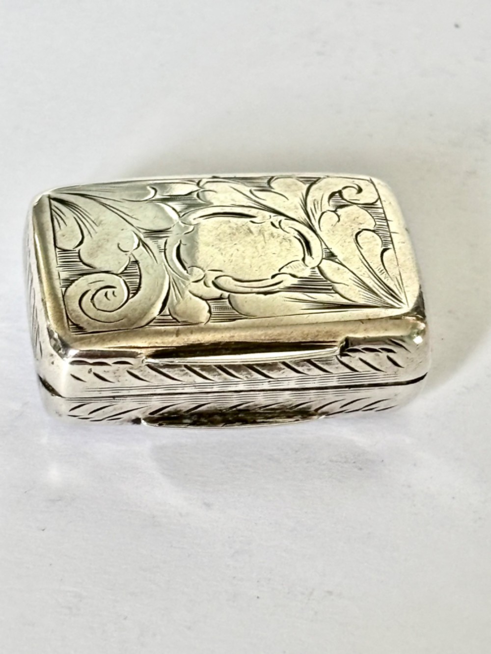 An early Victorian rectangular sterling silver vinaigrette featuring intricate foliate scroll engraving and a central unengraved cartouche. View VII