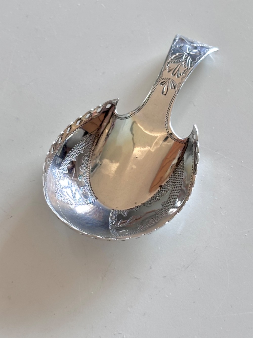 A Georgian sterling silver caddy spoon featuring a pastern hoof shaped bowl with bright-cut engraved decoration and a short handle.