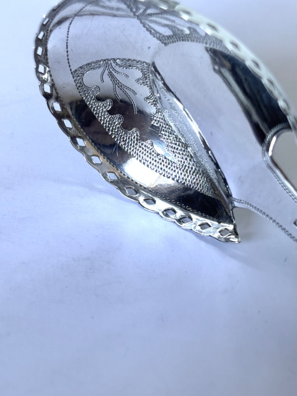 A Georgian sterling silver caddy spoon featuring a pastern hoof shaped bowl with bright-cut engraved decoration and a short handle. View II