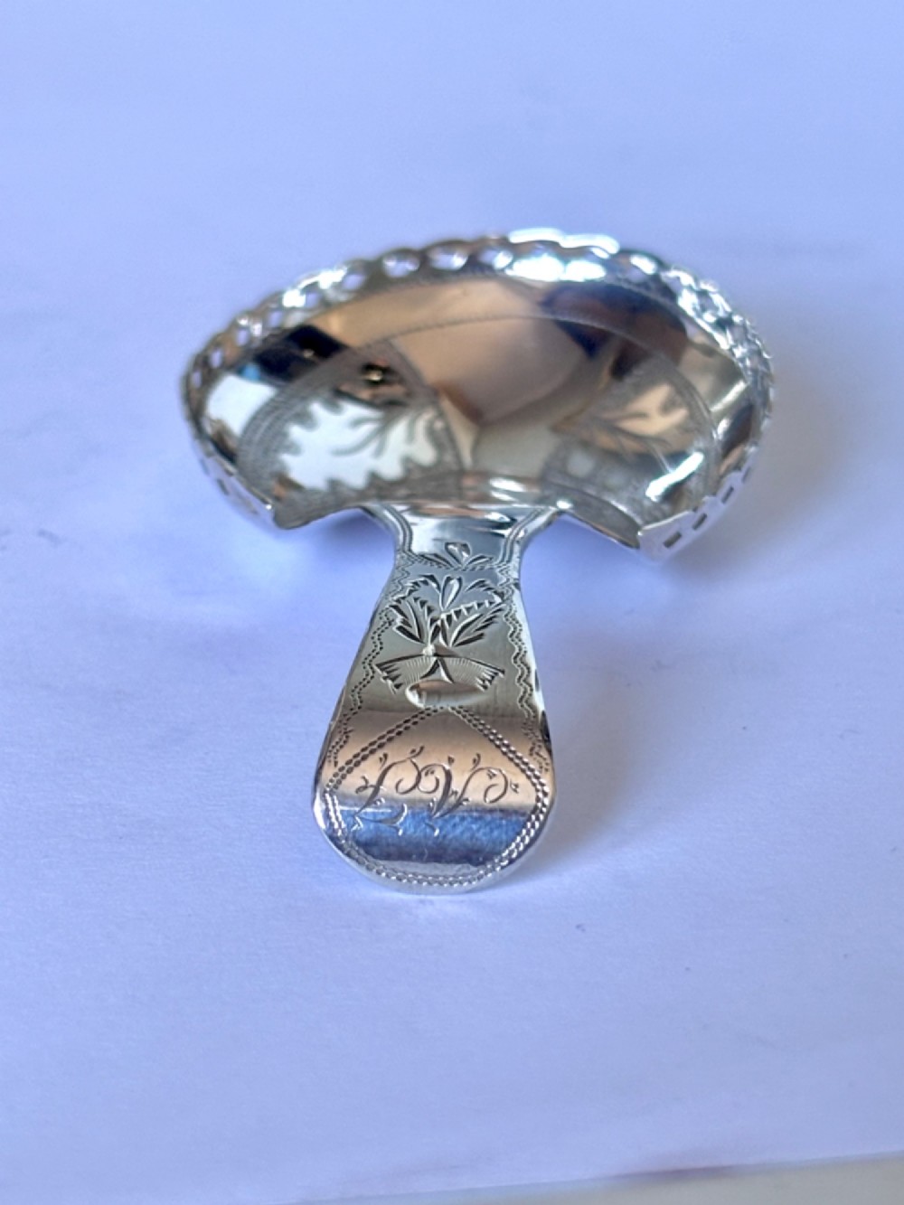 A Georgian sterling silver caddy spoon featuring a pastern hoof shaped bowl with bright-cut engraved decoration and a short handle. View IV