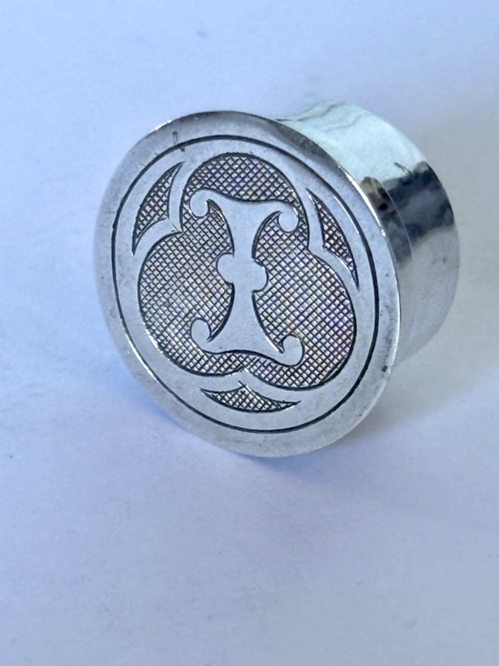 A circular sterling silver pyx box featuring an engraved monogram set against a textured hatch pattern on the lid.