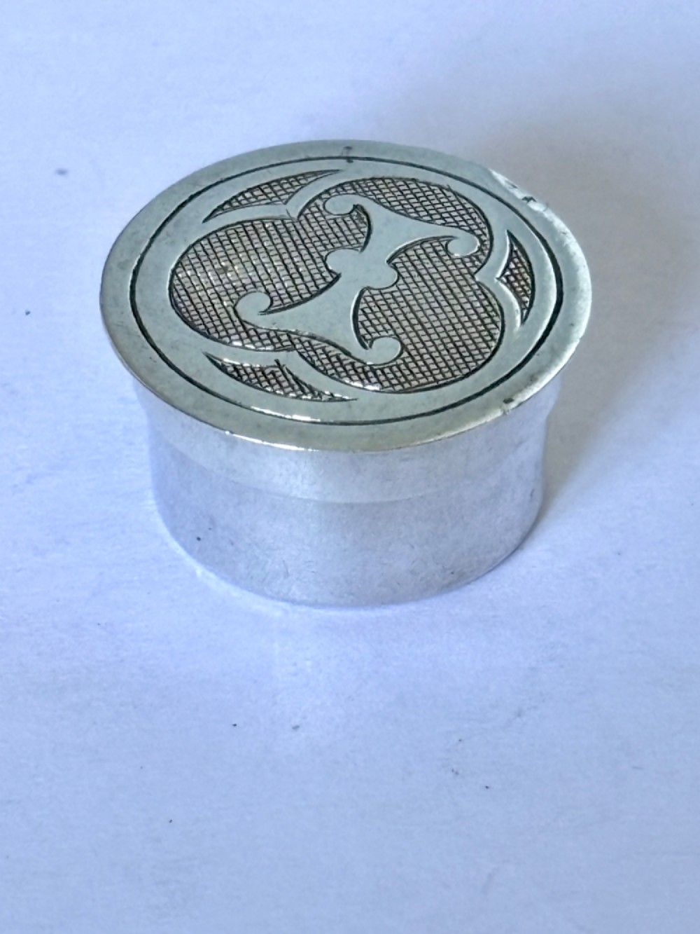 A circular sterling silver pyx box featuring an engraved monogram set against a textured hatch pattern on the lid. View II
