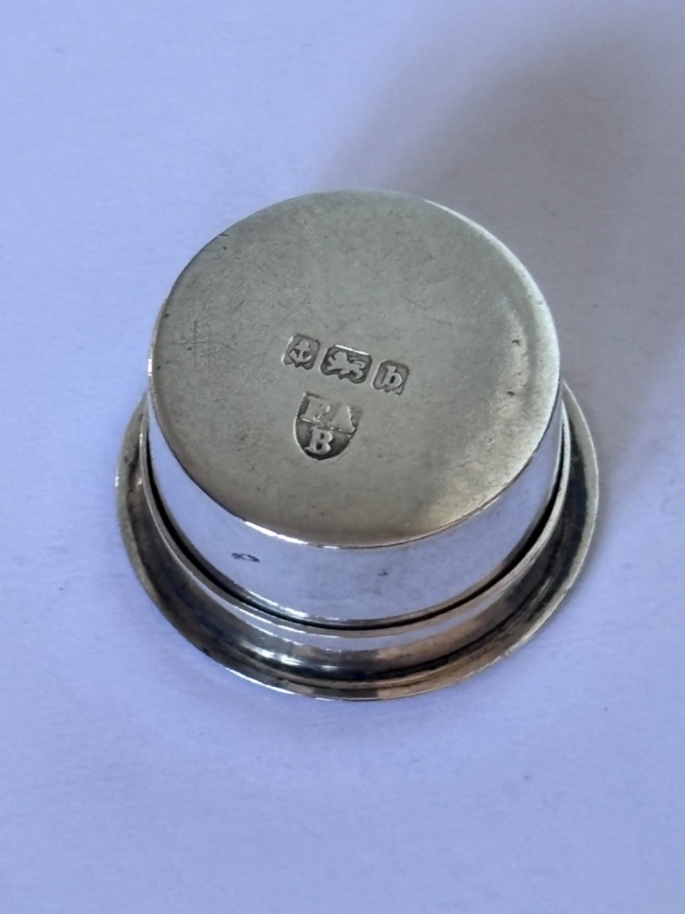 A circular sterling silver pyx box featuring an engraved monogram set against a textured hatch pattern on the lid. View III