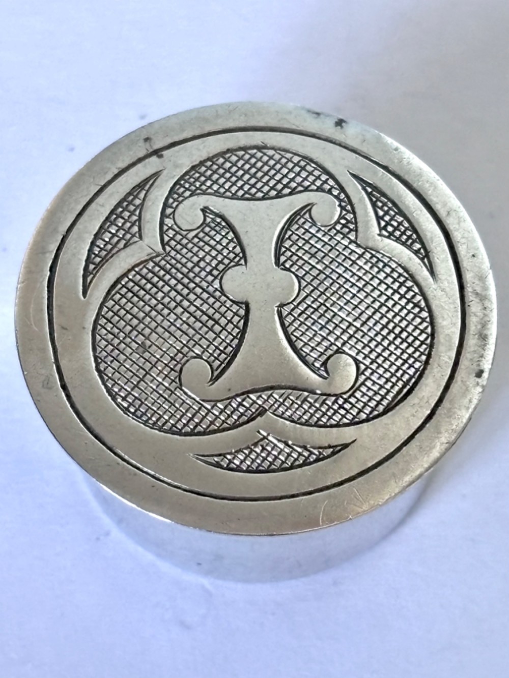 A circular sterling silver pyx box featuring an engraved monogram set against a textured hatch pattern on the lid. View V