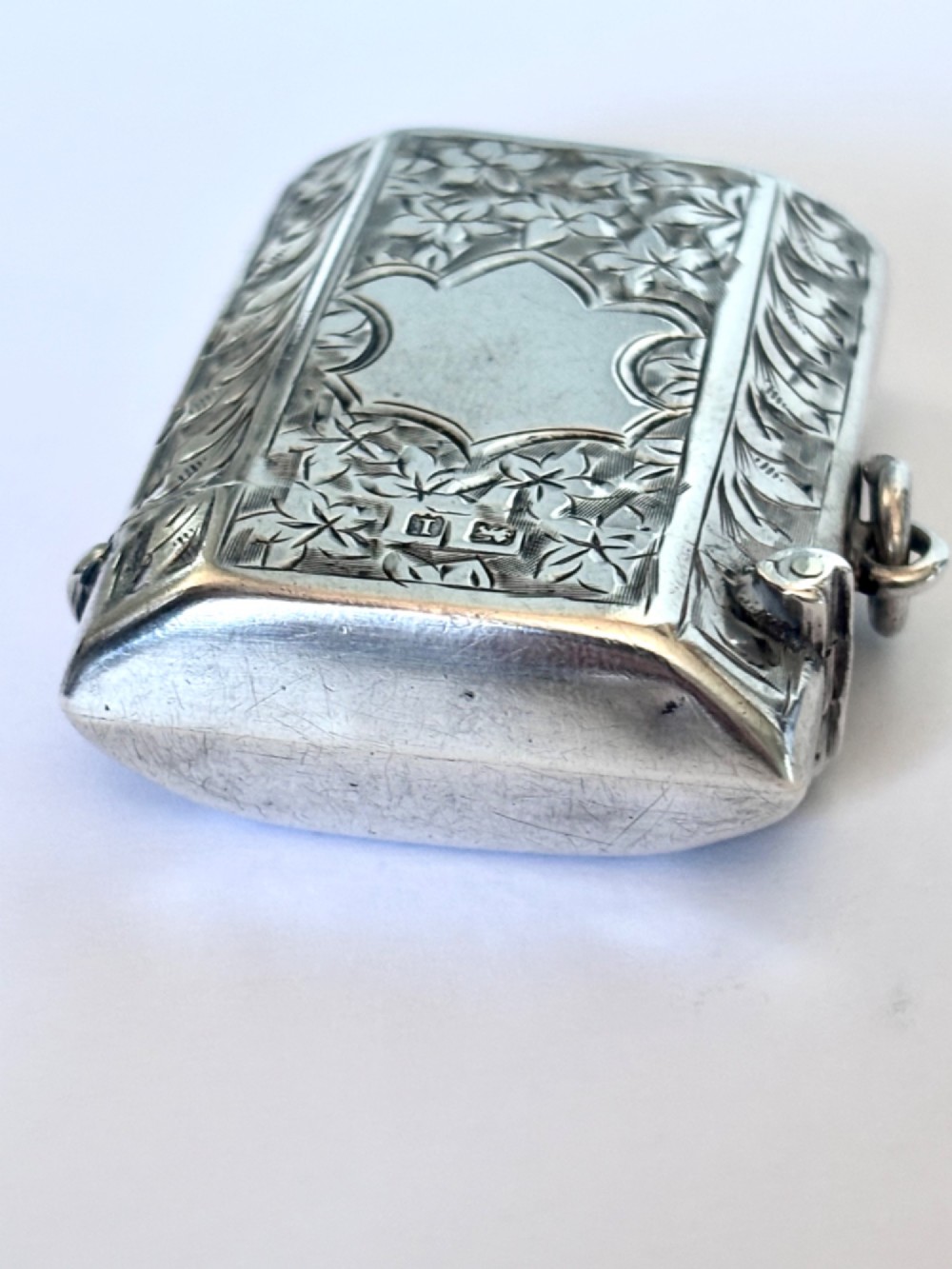 An engraved sterling silver vesta case featuring leaf motifs, a central vacant cartouche, a side suspension loop, and a base striker edge. View II