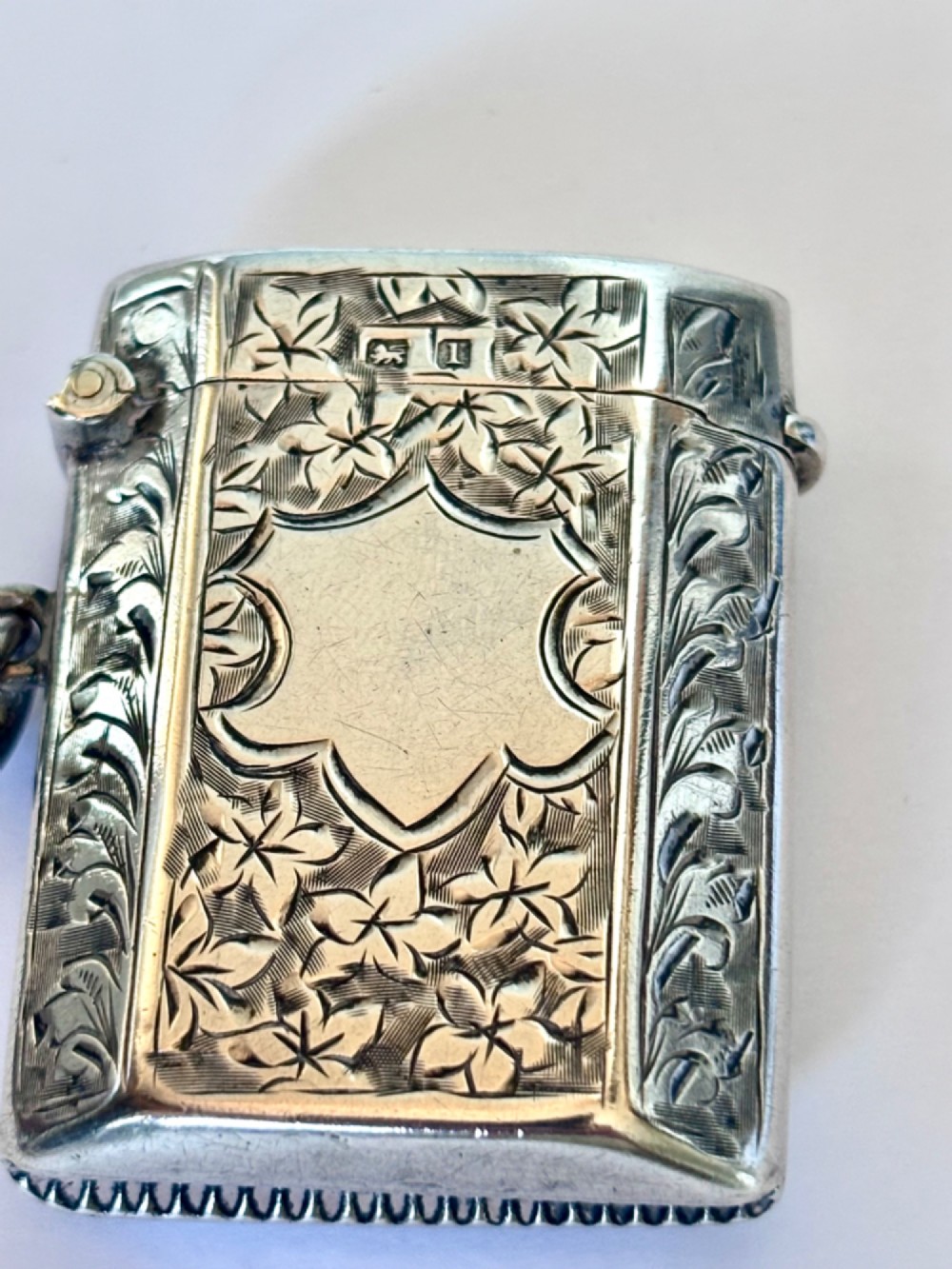An engraved sterling silver vesta case featuring leaf motifs, a central vacant cartouche, a side suspension loop, and a base striker edge. View VIII