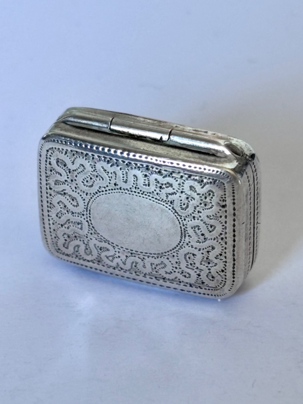 A small rectangular Georgian silver vinaigrette box with hand-engraved wrigglework patterns and a plain central oval cartouche.