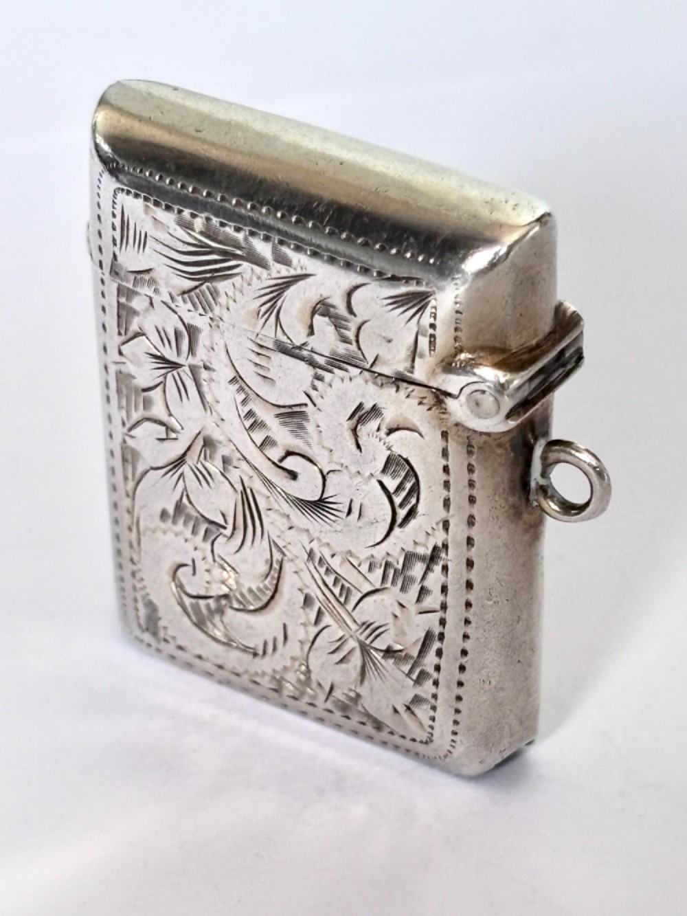 A rectangular Victorian sterling silver vesta case featuring hand-engraved scrollwork, a vacant central cartouche, and a side attachment ring. View II
