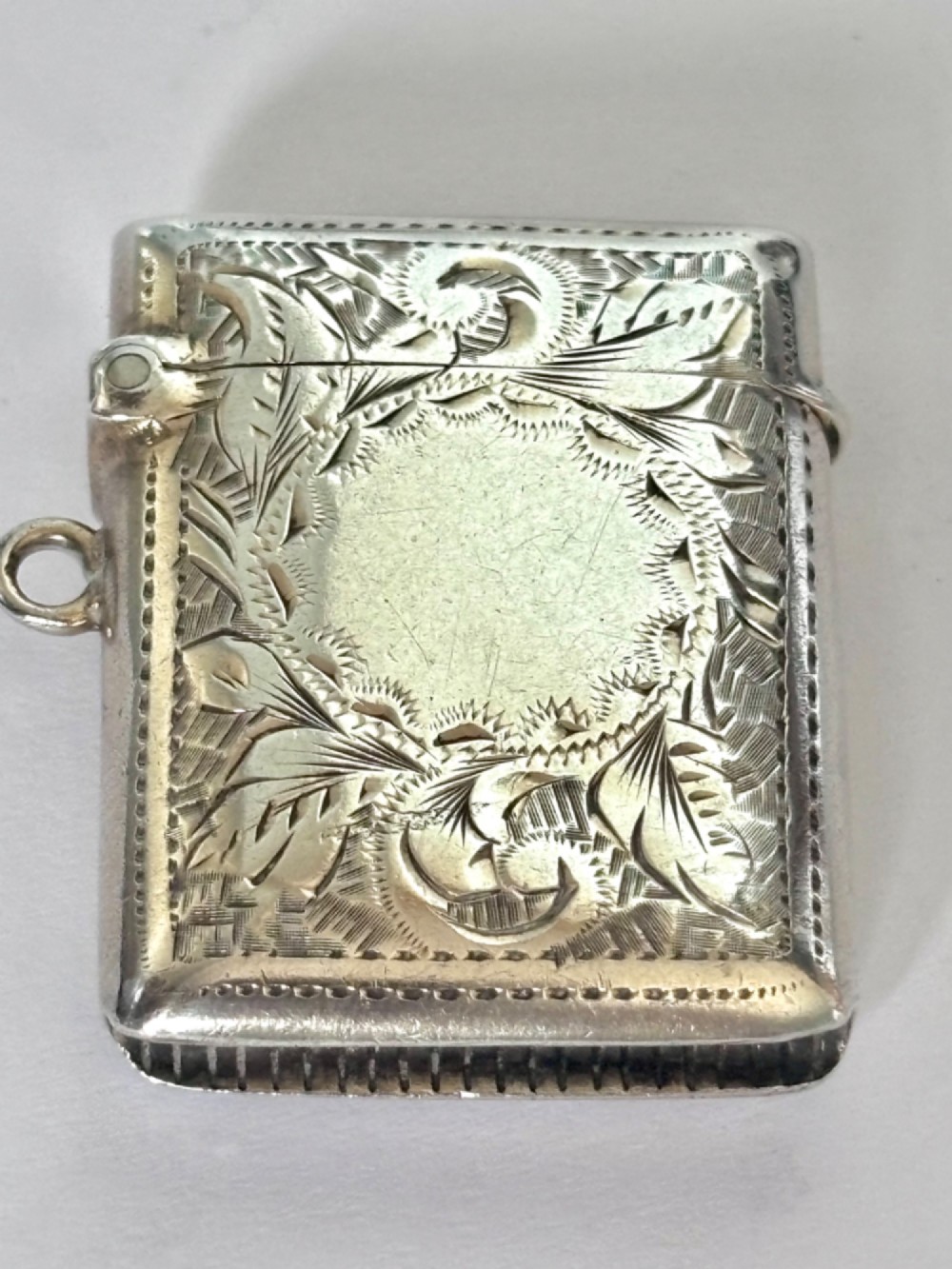 A rectangular Victorian sterling silver vesta case featuring hand-engraved scrollwork, a vacant central cartouche, and a side attachment ring. View III