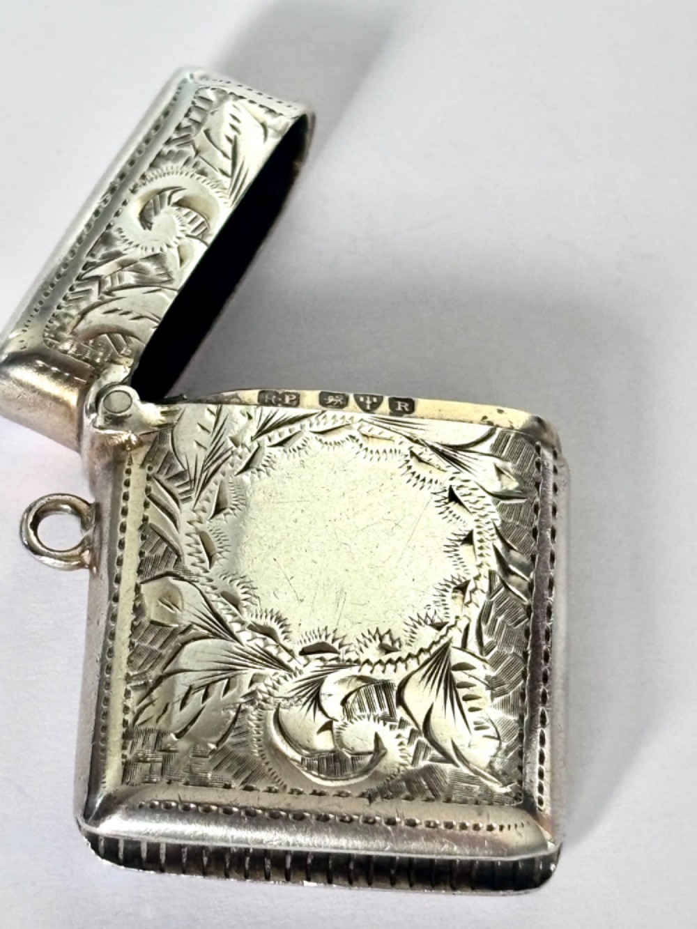 A rectangular Victorian sterling silver vesta case featuring hand-engraved scrollwork, a vacant central cartouche, and a side attachment ring. View V