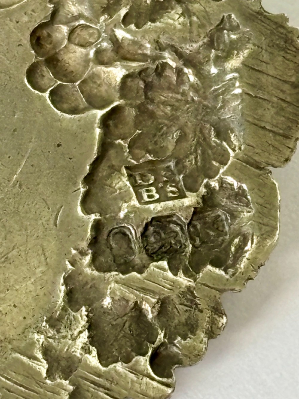A George III sterling silver decanter label engraved with MADEIRA, decorated with a chased mask of Bacchus, grapevines, and an attached suspension chain. View II
