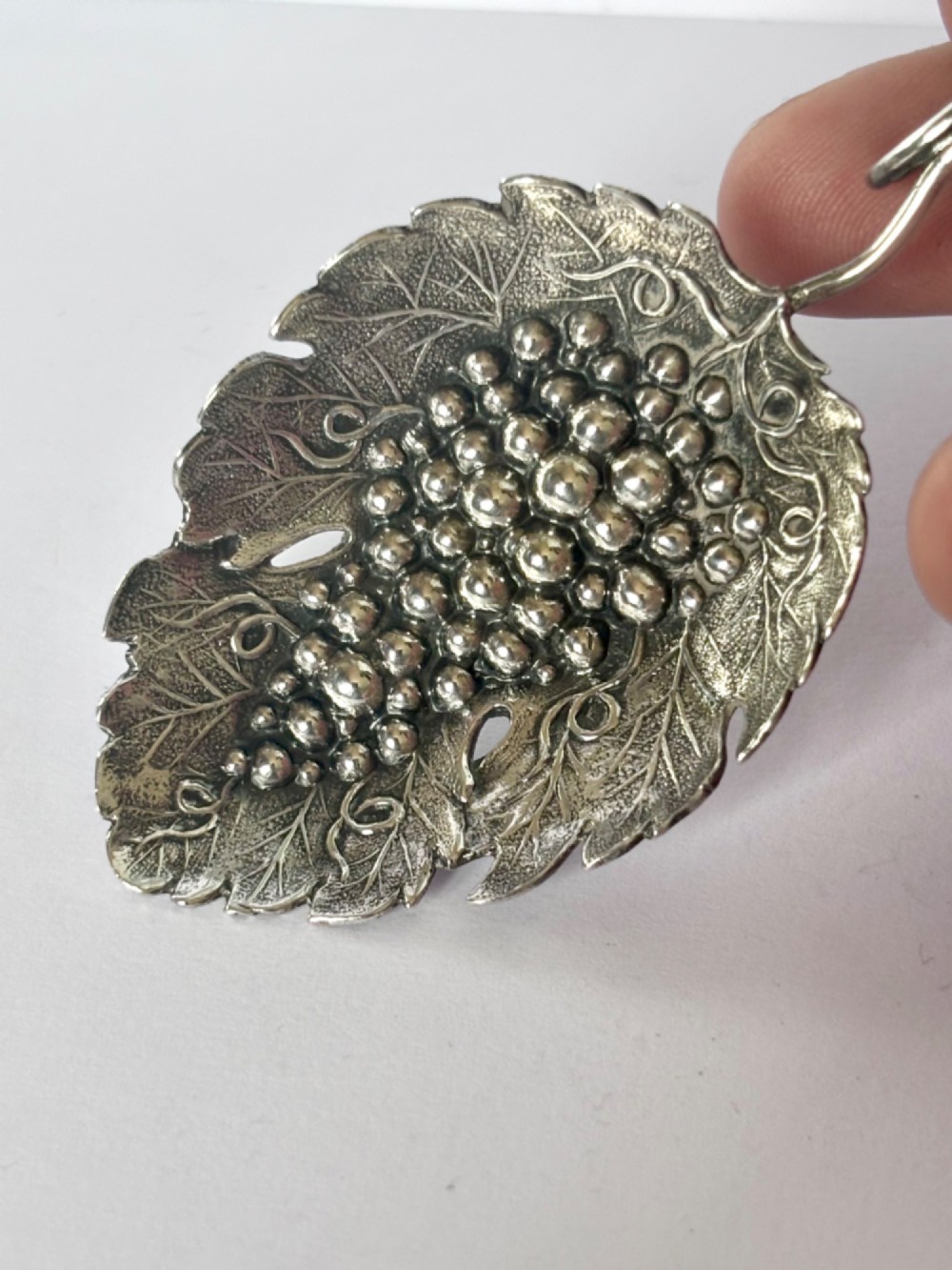 A George III sterling silver caddy spoon fashioned as a vine leaf with an embossed grape cluster and a wire loop handle. View III