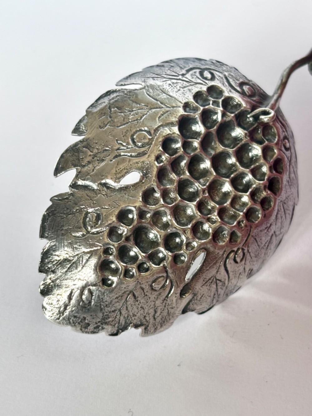A George III sterling silver caddy spoon fashioned as a vine leaf with an embossed grape cluster and a wire loop handle. View IV