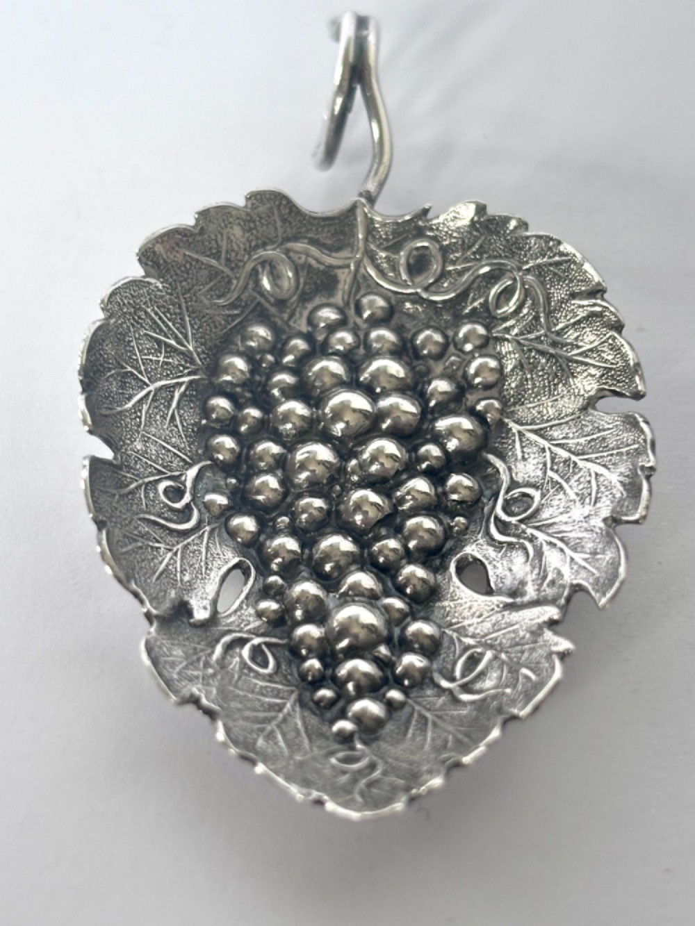 A George III sterling silver caddy spoon fashioned as a vine leaf with an embossed grape cluster and a wire loop handle. View V