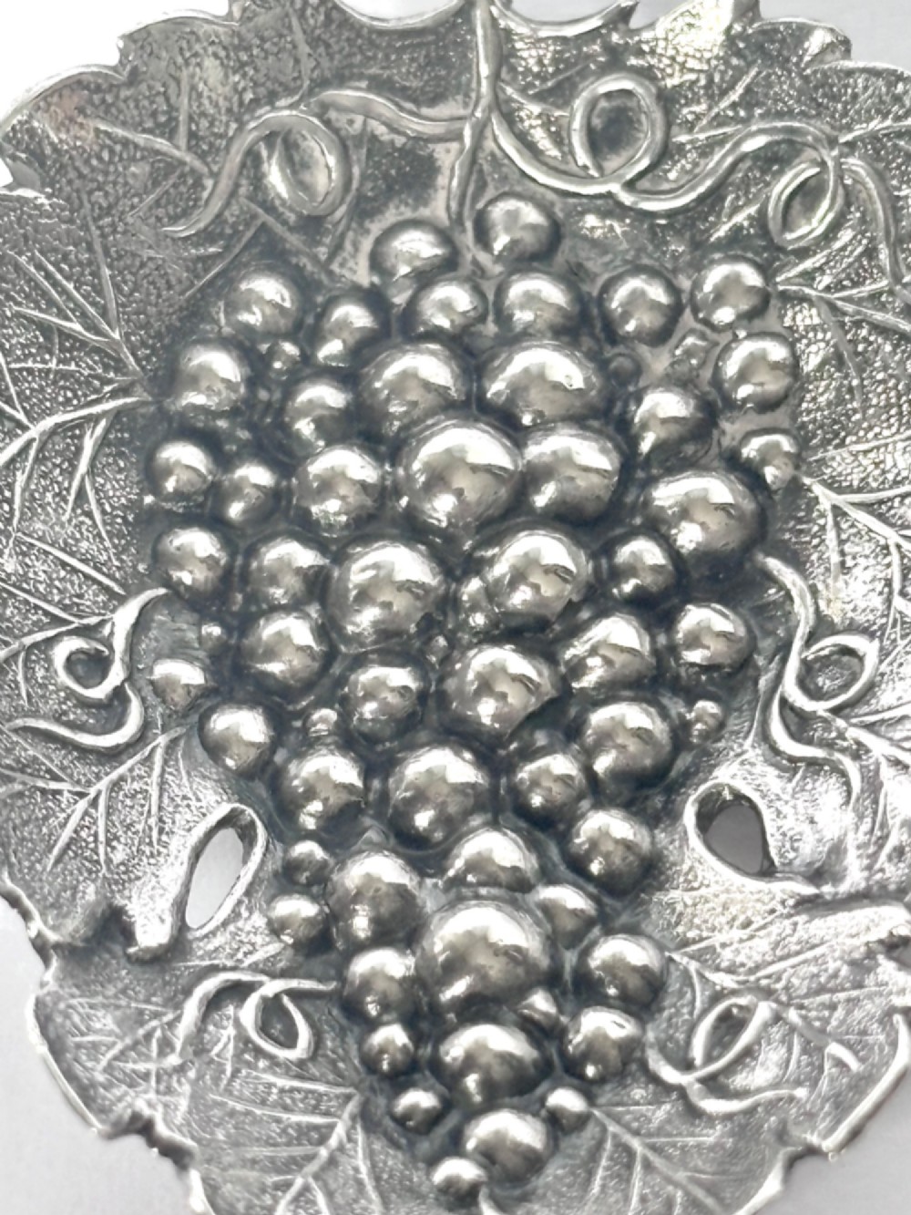 A George III sterling silver caddy spoon fashioned as a vine leaf with an embossed grape cluster and a wire loop handle. View VI