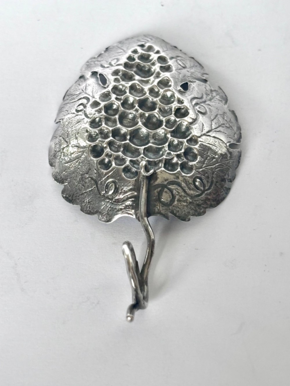 A George III sterling silver caddy spoon fashioned as a vine leaf with an embossed grape cluster and a wire loop handle. View XI