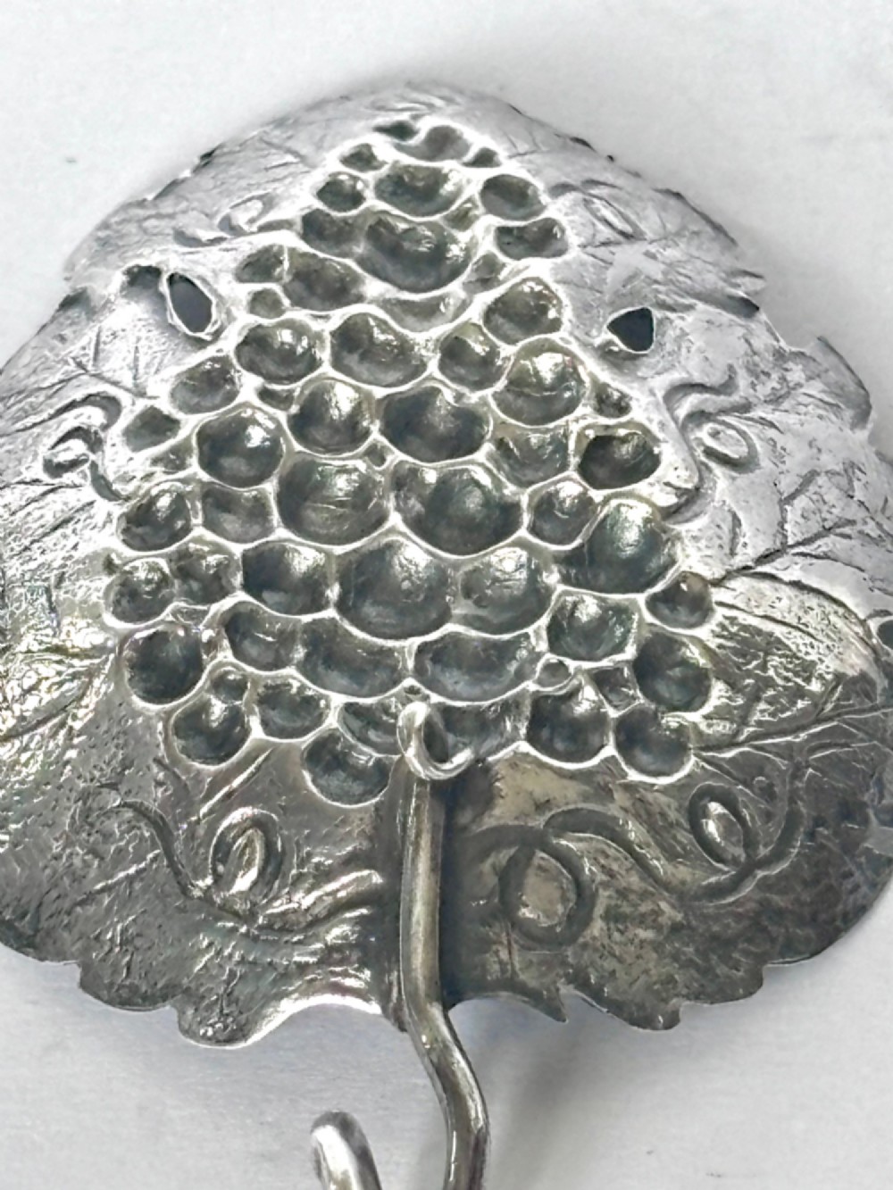 A George III sterling silver caddy spoon fashioned as a vine leaf with an embossed grape cluster and a wire loop handle. View XII