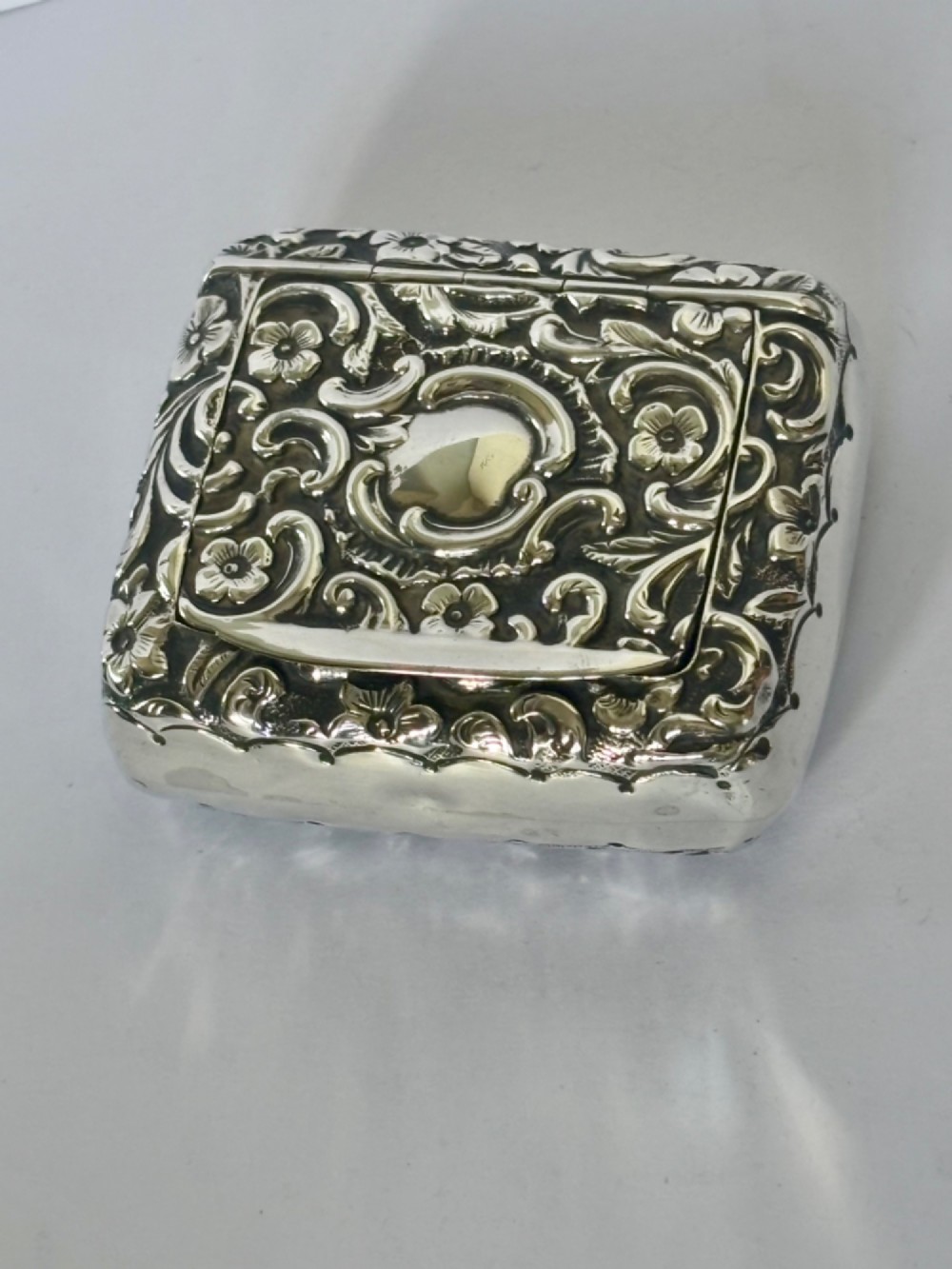 A Victorian rectangular sterling silver snuff box with heavily embossed floral and scroll decoration surrounding a plain central cartouche. View II