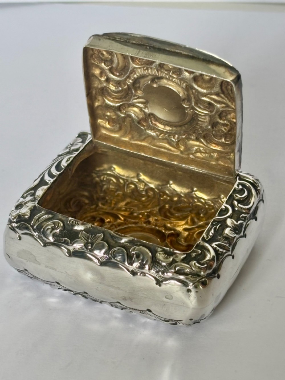 A Victorian rectangular sterling silver snuff box with heavily embossed floral and scroll decoration surrounding a plain central cartouche. View III