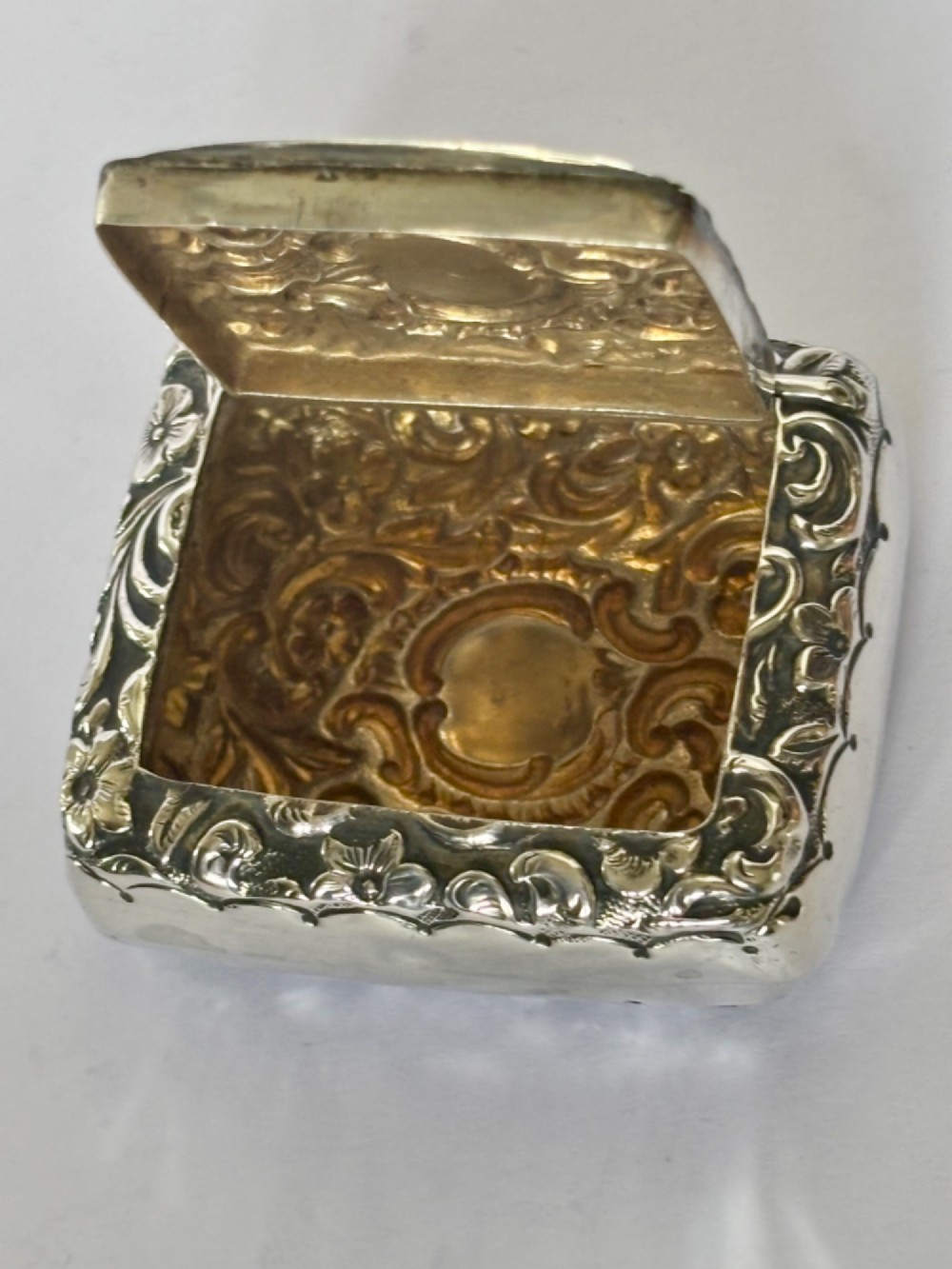 A Victorian rectangular sterling silver snuff box with heavily embossed floral and scroll decoration surrounding a plain central cartouche. View IV