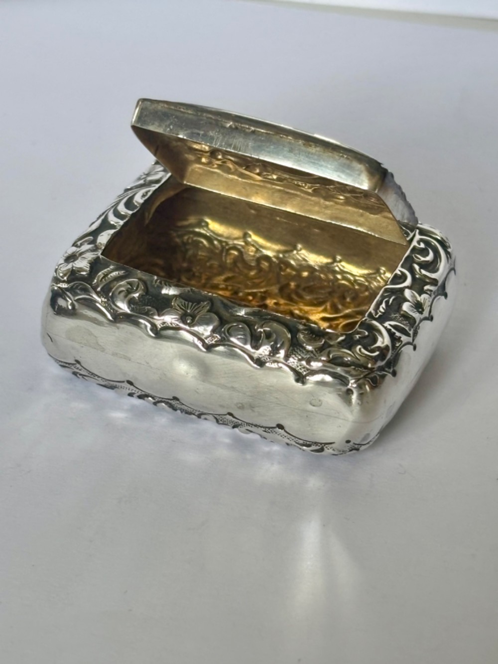 A Victorian rectangular sterling silver snuff box with heavily embossed floral and scroll decoration surrounding a plain central cartouche. View VII
