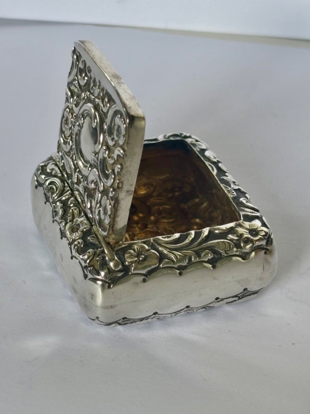 A Victorian rectangular sterling silver snuff box with heavily embossed floral and scroll decoration surrounding a plain central cartouche. View VIII
