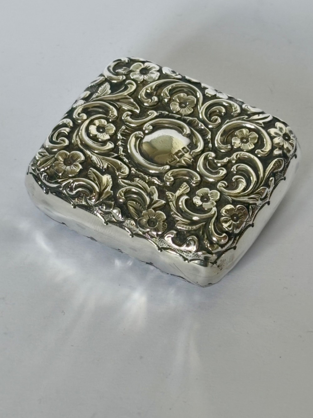 A Victorian rectangular sterling silver snuff box with heavily embossed floral and scroll decoration surrounding a plain central cartouche. View IX