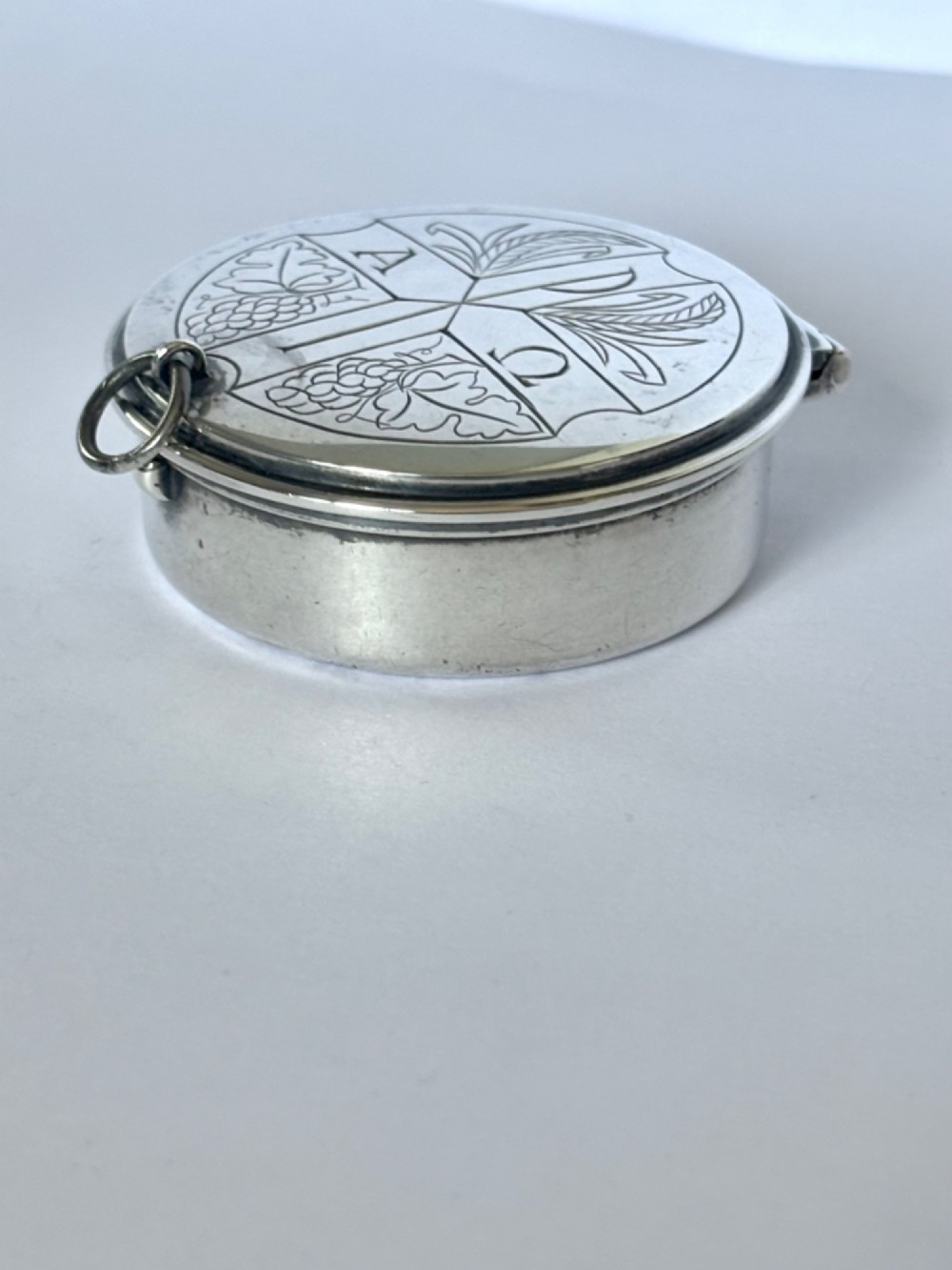 A small round sterling silver pyx box shown open, featuring a silver exterior and a gold-gilt interior stamped with hallmarks. View II