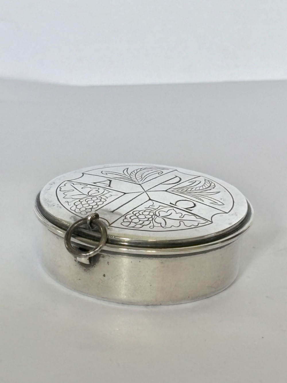 A small round sterling silver pyx box shown open, featuring a silver exterior and a gold-gilt interior stamped with hallmarks. View V