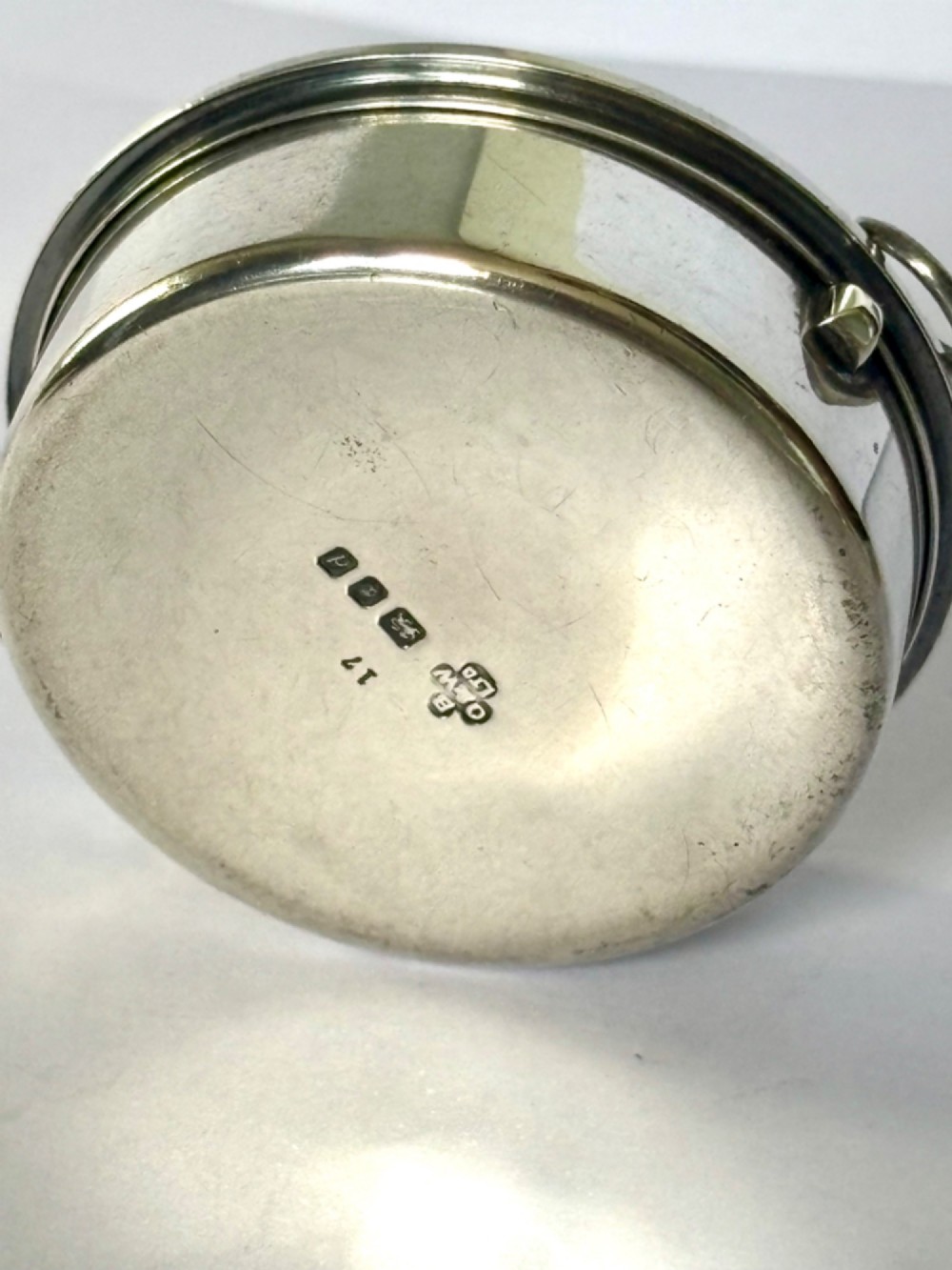 A small round sterling silver pyx box shown open, featuring a silver exterior and a gold-gilt interior stamped with hallmarks. View VI