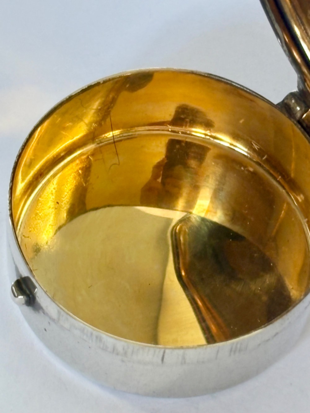 A small round sterling silver pyx box shown open, featuring a silver exterior and a gold-gilt interior stamped with hallmarks. View VII