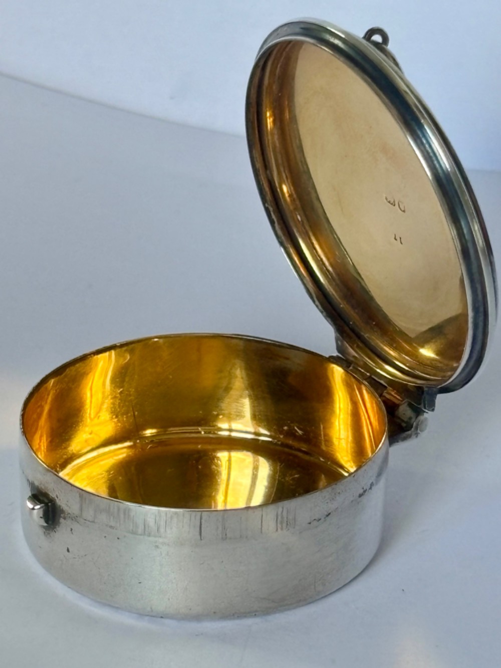 A small round sterling silver pyx box shown open, featuring a silver exterior and a gold-gilt interior stamped with hallmarks. View VIII
