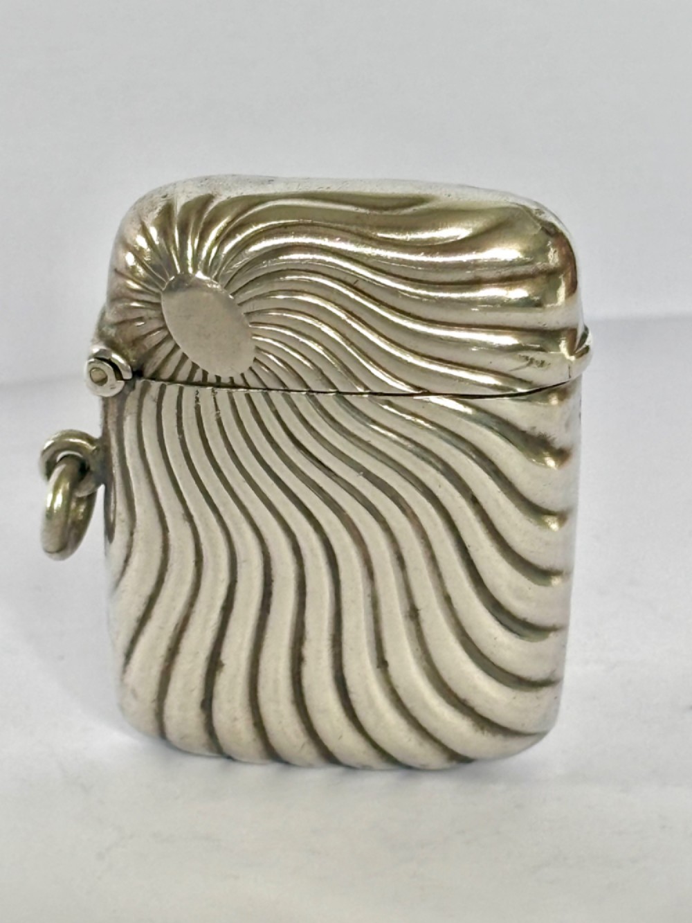 An Edwardian sterling silver pocket vesta case featuring a raised sunburst design with radiating swirled fluting and a side suspension ring. View II
