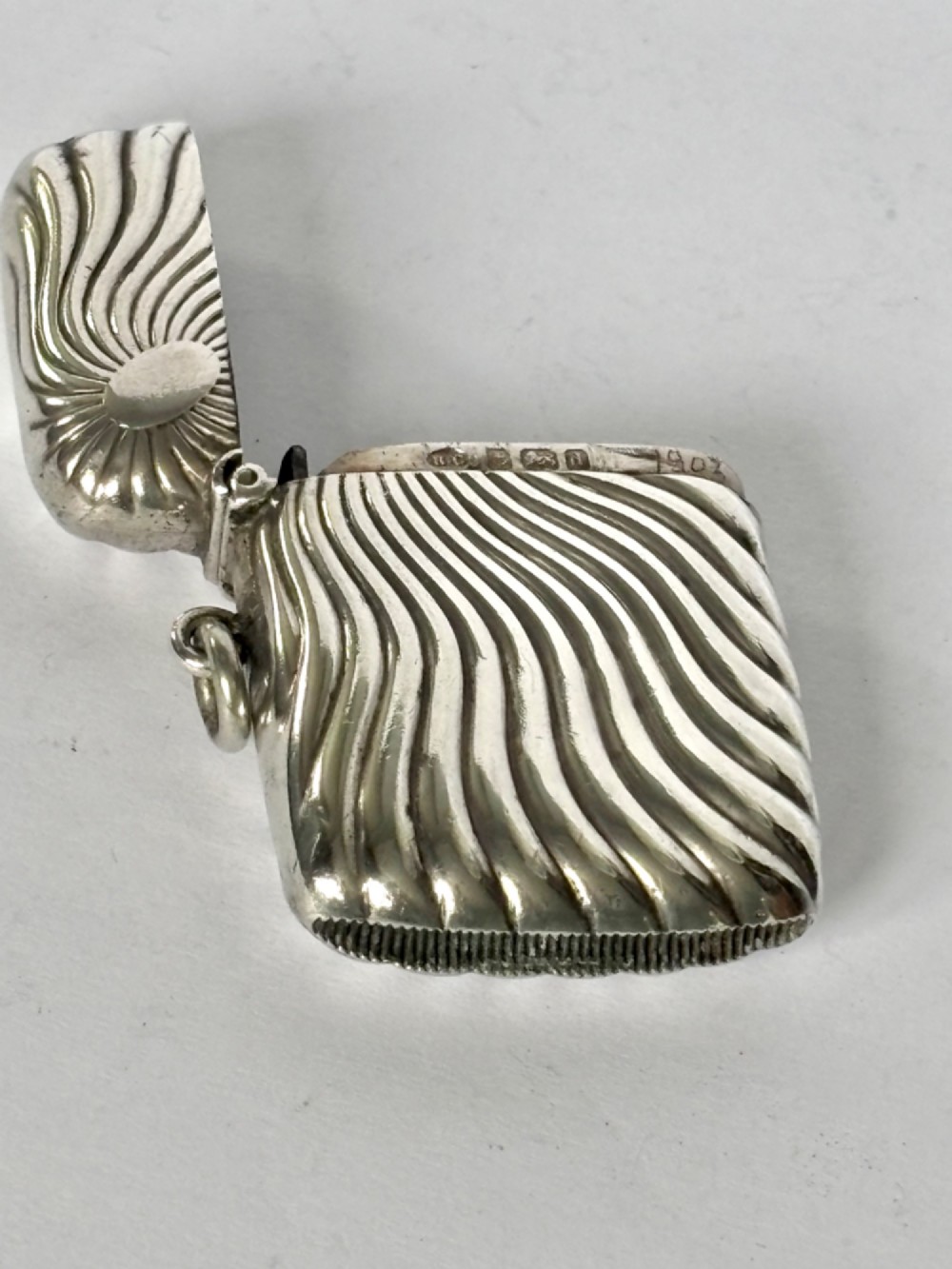 An Edwardian sterling silver pocket vesta case featuring a raised sunburst design with radiating swirled fluting and a side suspension ring. View V