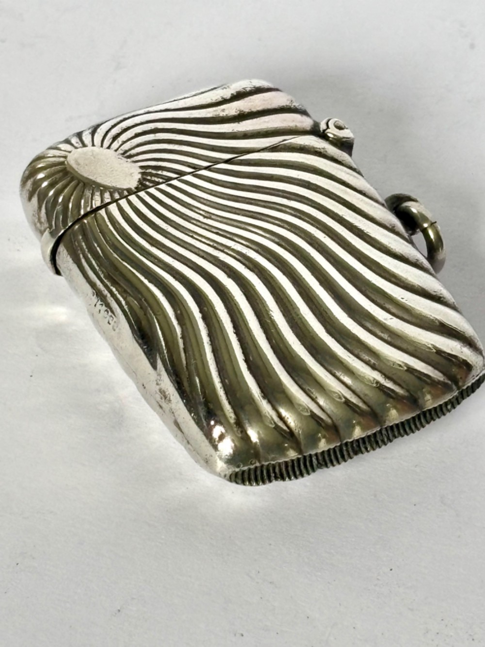 An Edwardian sterling silver pocket vesta case featuring a raised sunburst design with radiating swirled fluting and a side suspension ring. View VII
