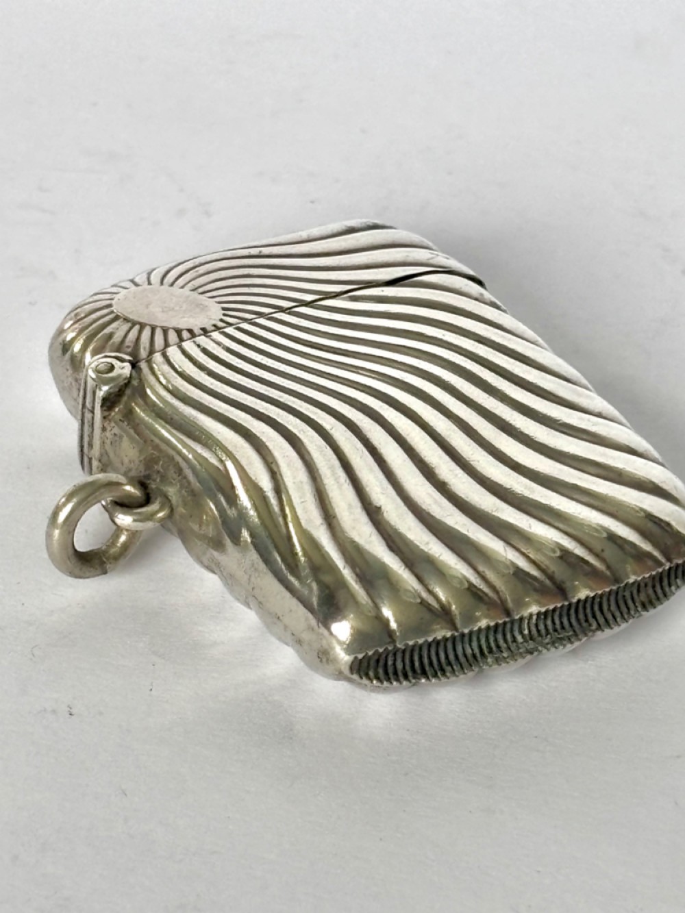 An Edwardian sterling silver pocket vesta case featuring a raised sunburst design with radiating swirled fluting and a side suspension ring. View VIII