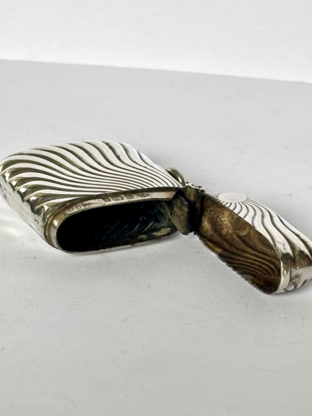An Edwardian sterling silver pocket vesta case featuring a raised sunburst design with radiating swirled fluting and a side suspension ring. View IX