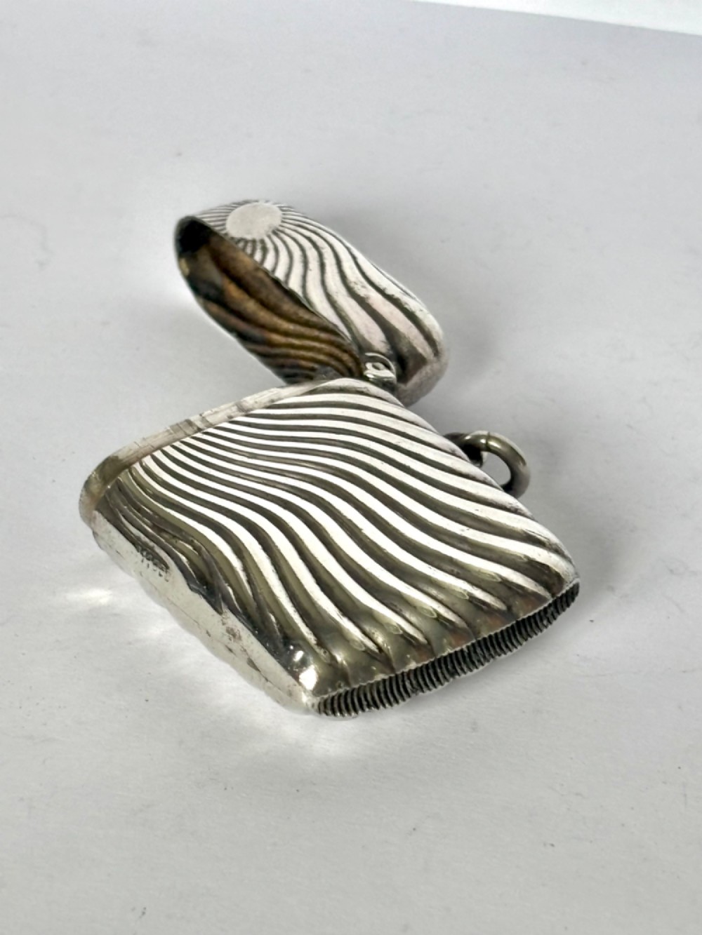An Edwardian sterling silver pocket vesta case featuring a raised sunburst design with radiating swirled fluting and a side suspension ring. View X