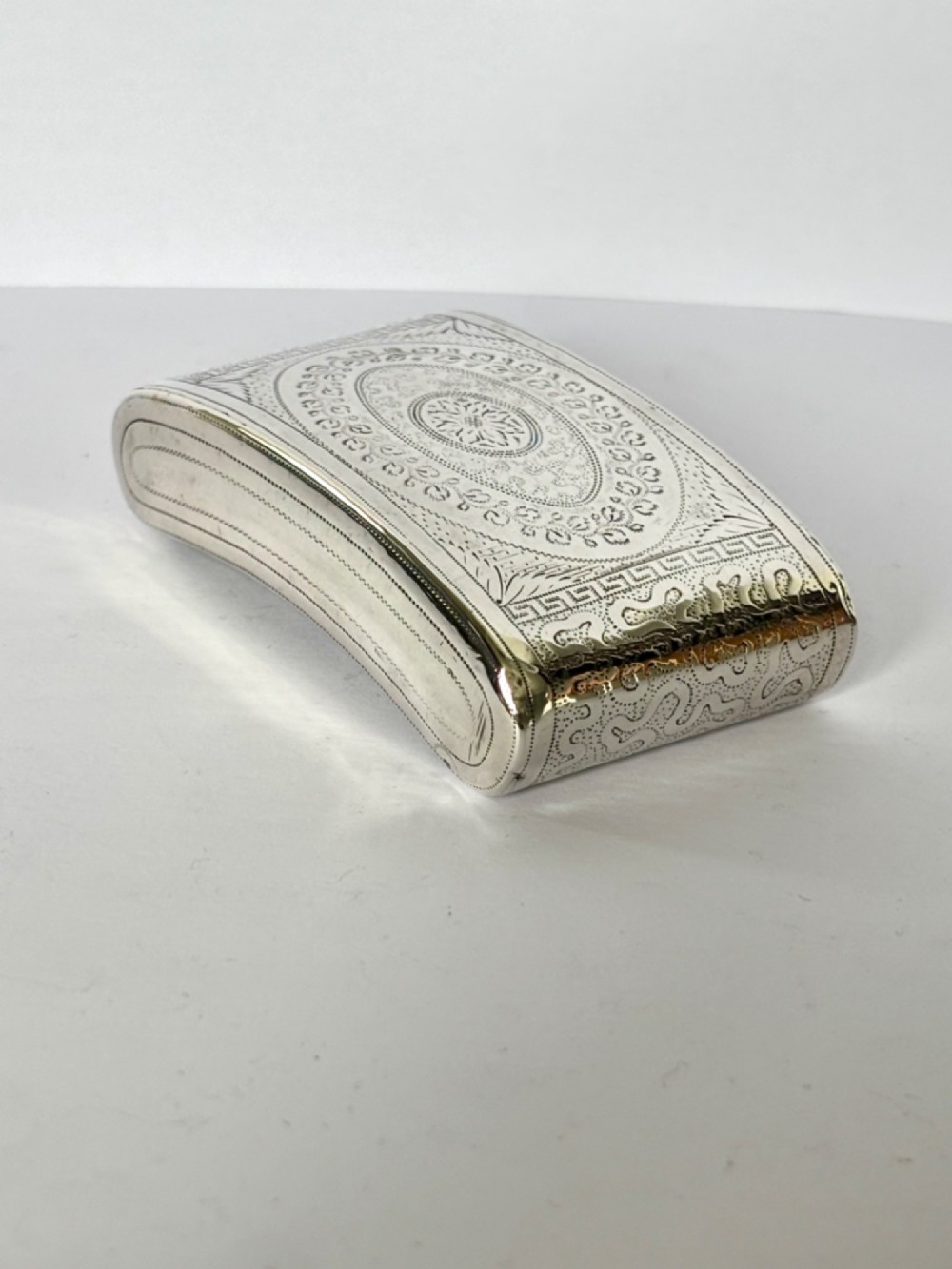 A curved antique sterling silver pocket snuff box featuring elaborate hand engraving and a flush hinge. View II