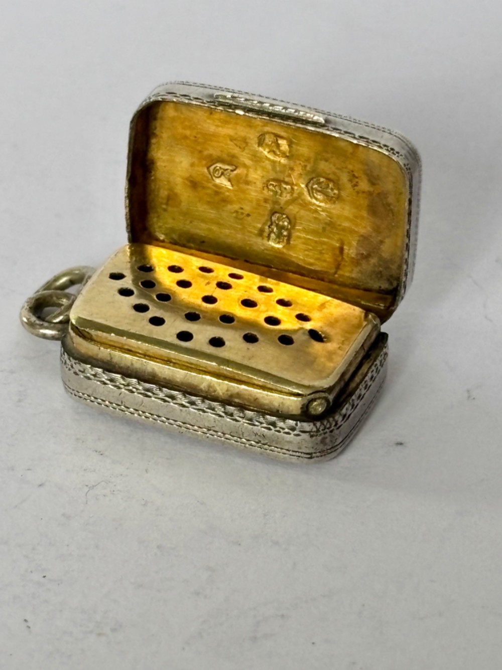 A small rectangular Georgian silver vinaigrette featuring intricate floral engraving, textured background patterns, and an attached suspension ring. View II