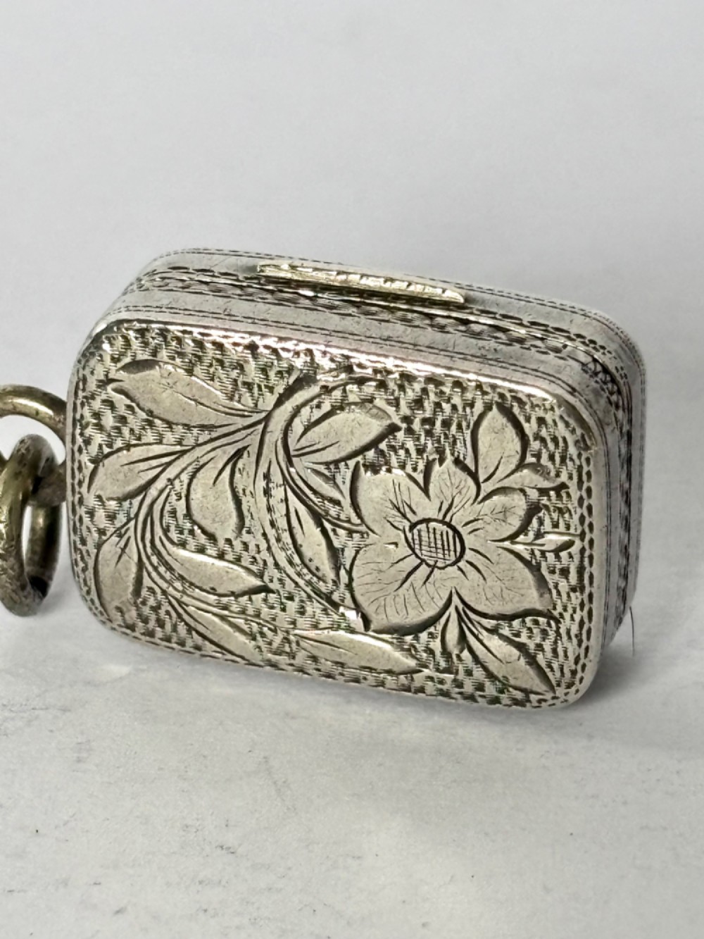 A small rectangular Georgian silver vinaigrette featuring intricate floral engraving, textured background patterns, and an attached suspension ring. View III