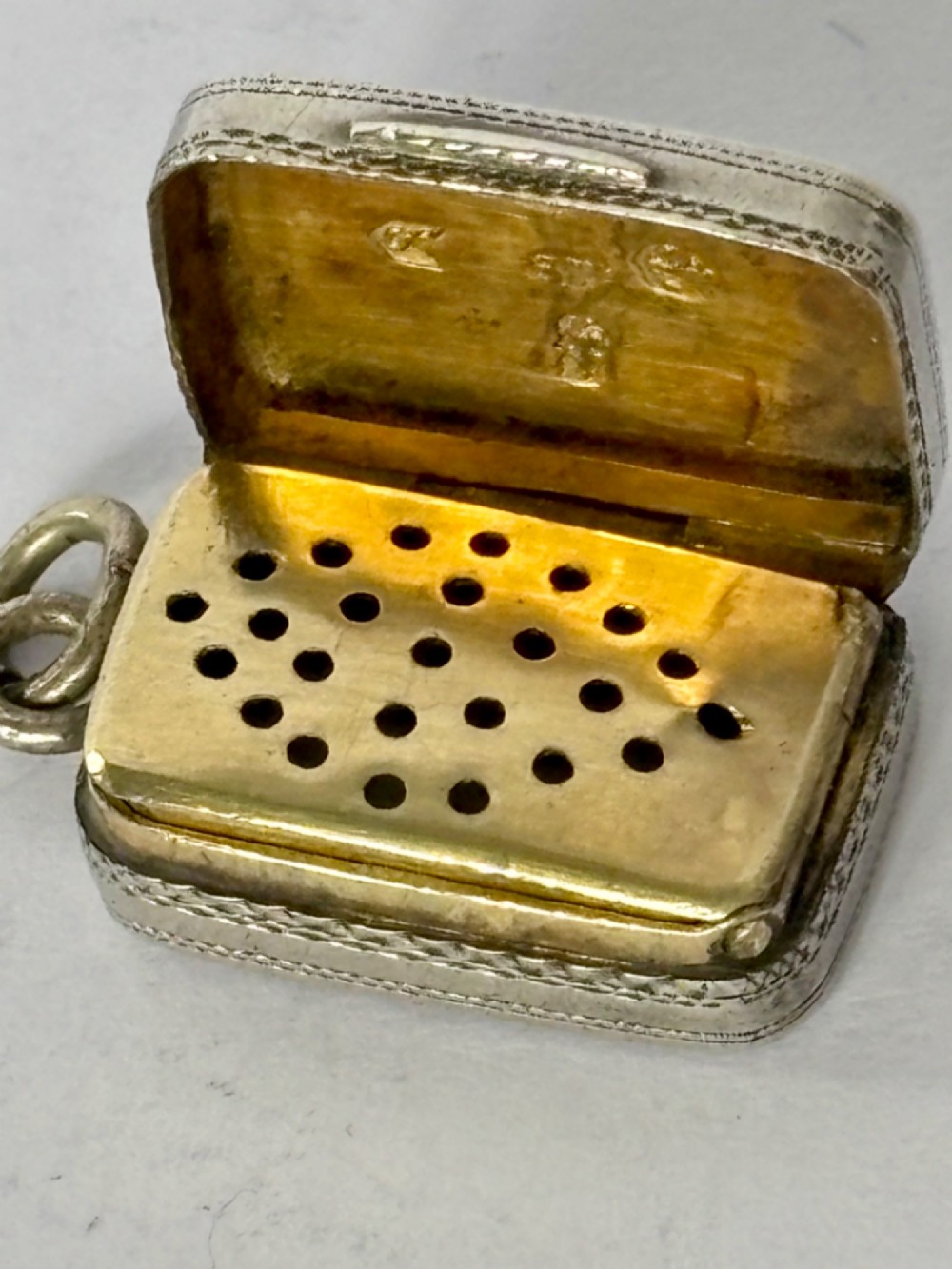 A small rectangular Georgian silver vinaigrette featuring intricate floral engraving, textured background patterns, and an attached suspension ring. View IV