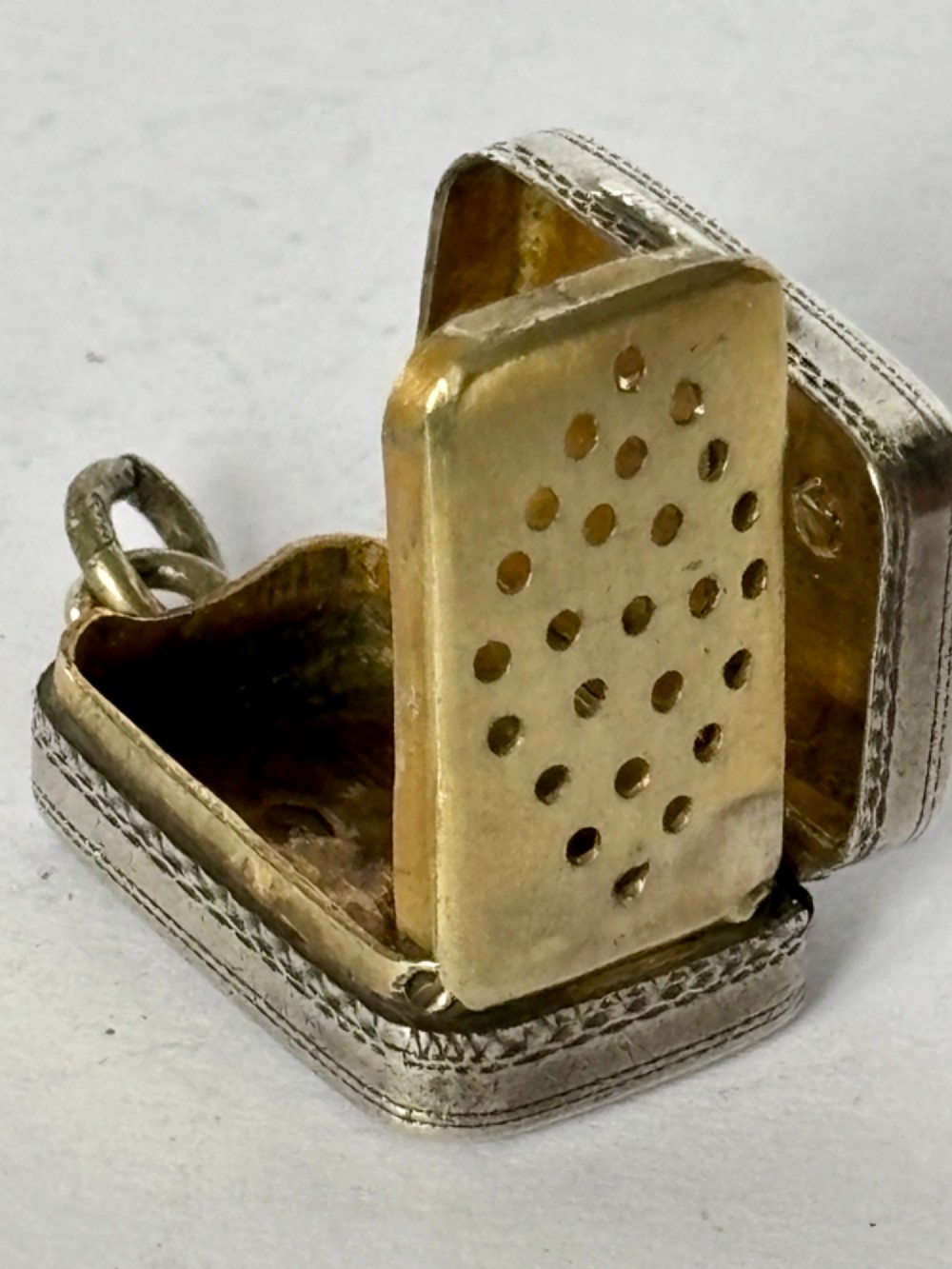 A small rectangular Georgian silver vinaigrette featuring intricate floral engraving, textured background patterns, and an attached suspension ring. View V