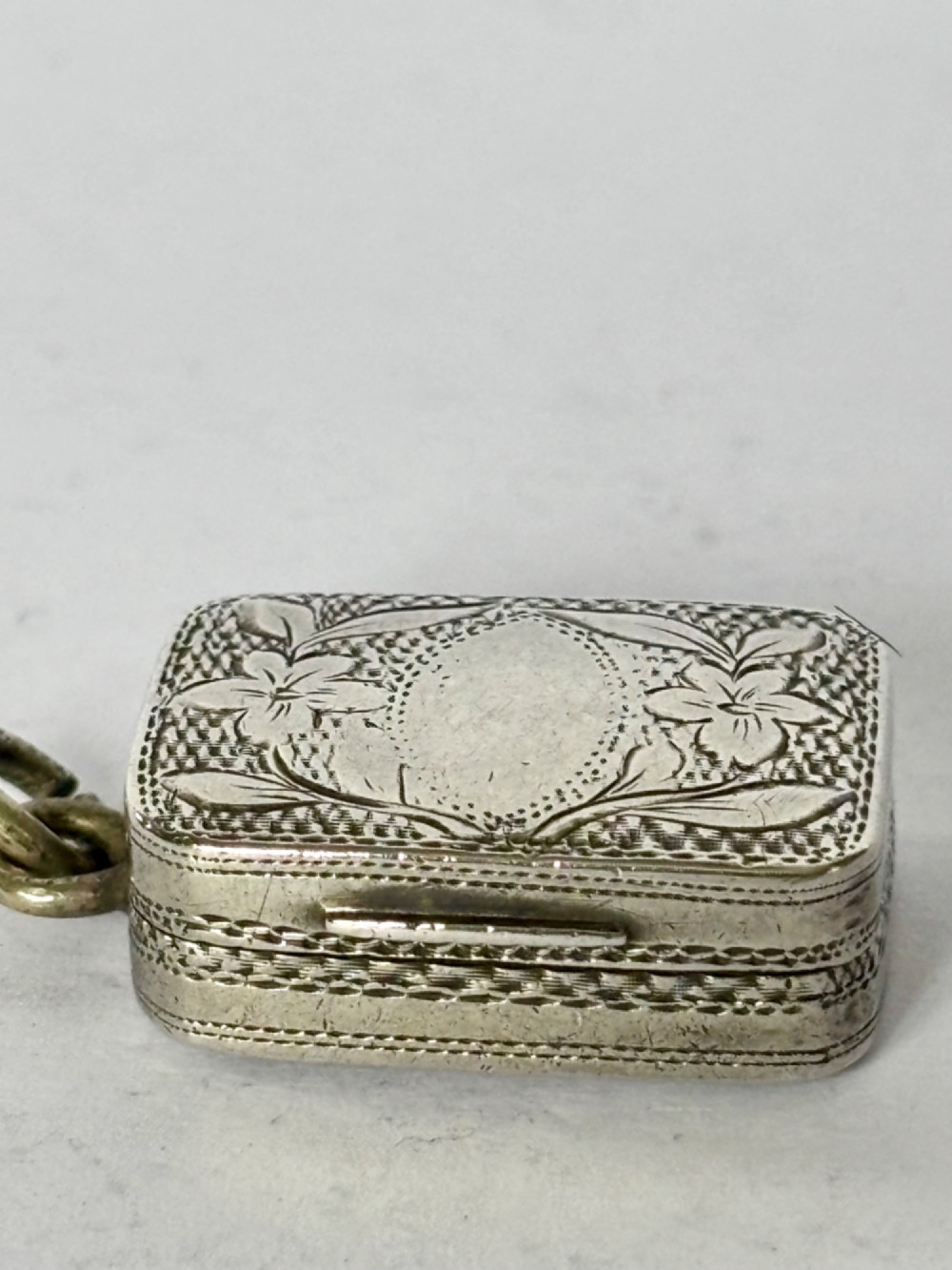 A small rectangular Georgian silver vinaigrette featuring intricate floral engraving, textured background patterns, and an attached suspension ring. View VII