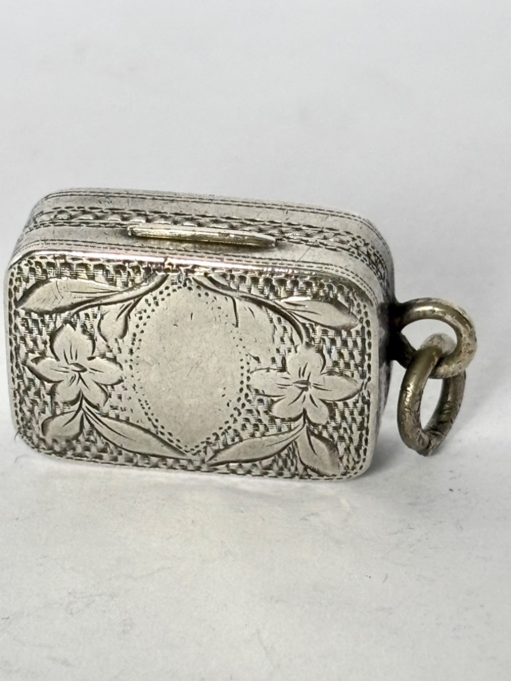 A small rectangular Georgian silver vinaigrette featuring intricate floral engraving, textured background patterns, and an attached suspension ring. View VIII