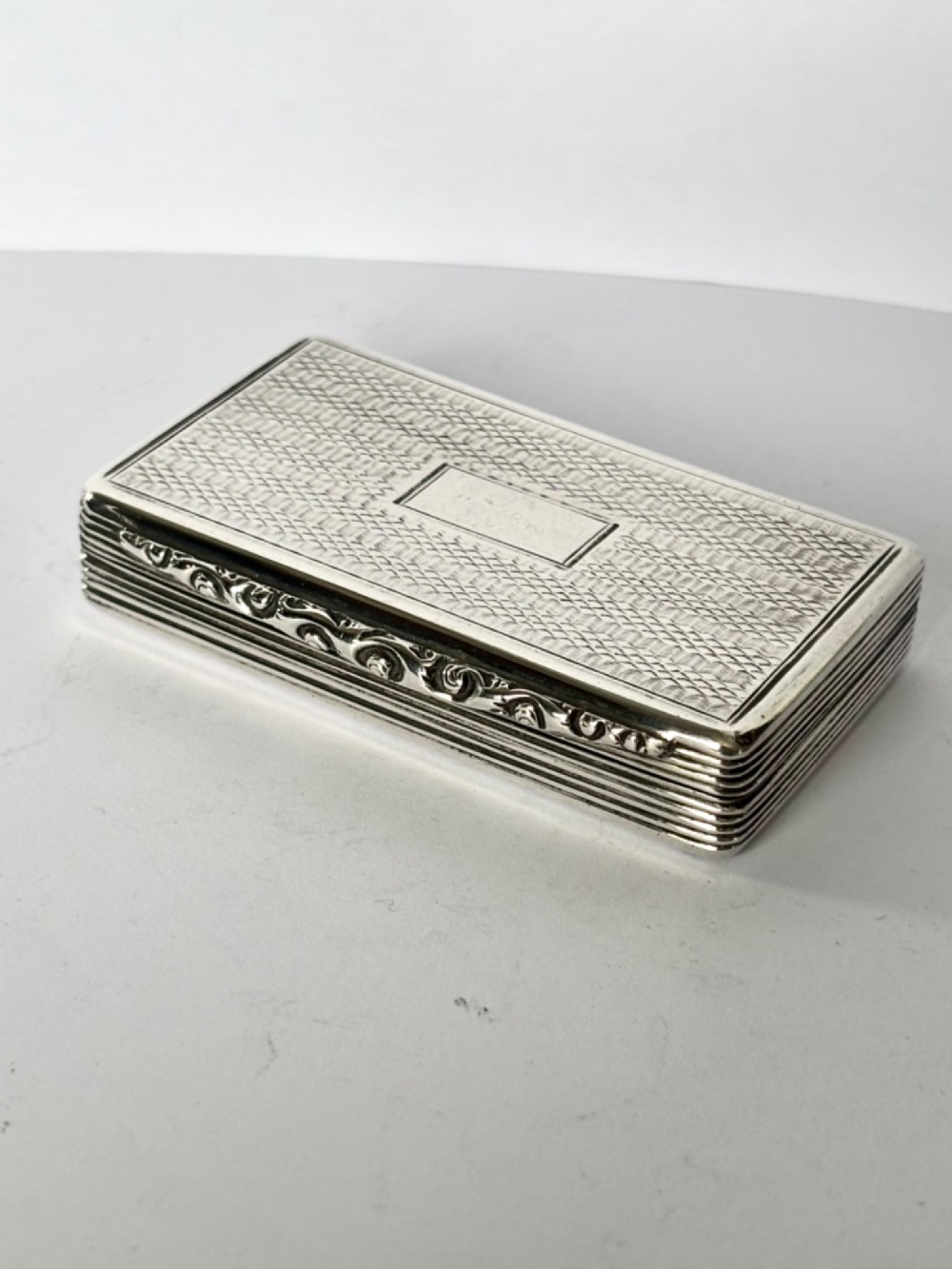 A rectangular Georgian sterling silver snuff box displaying geometric engine-turned patterns, a blank central cartouche, and reeded side edges.